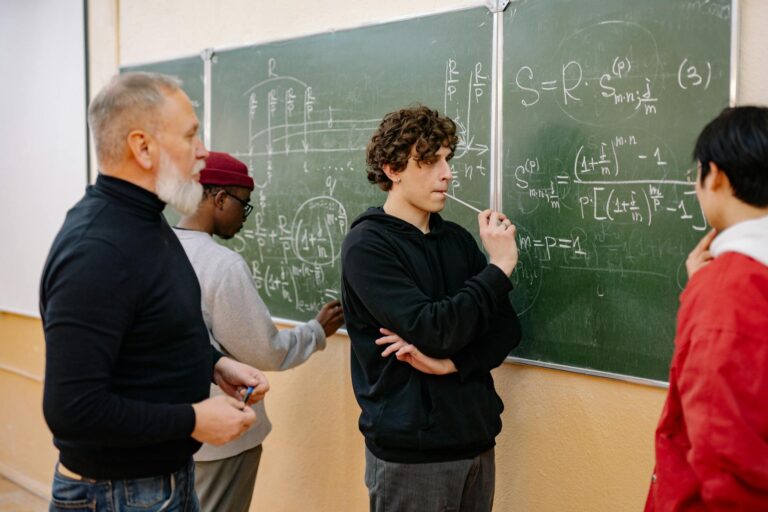 Group of students and professor discussing complex equations on a chalkboard.